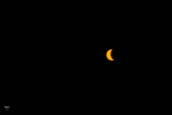 An orange crescent sun during a partial solar eclipse against a black sky. Photograph by Digital Life Concepts.